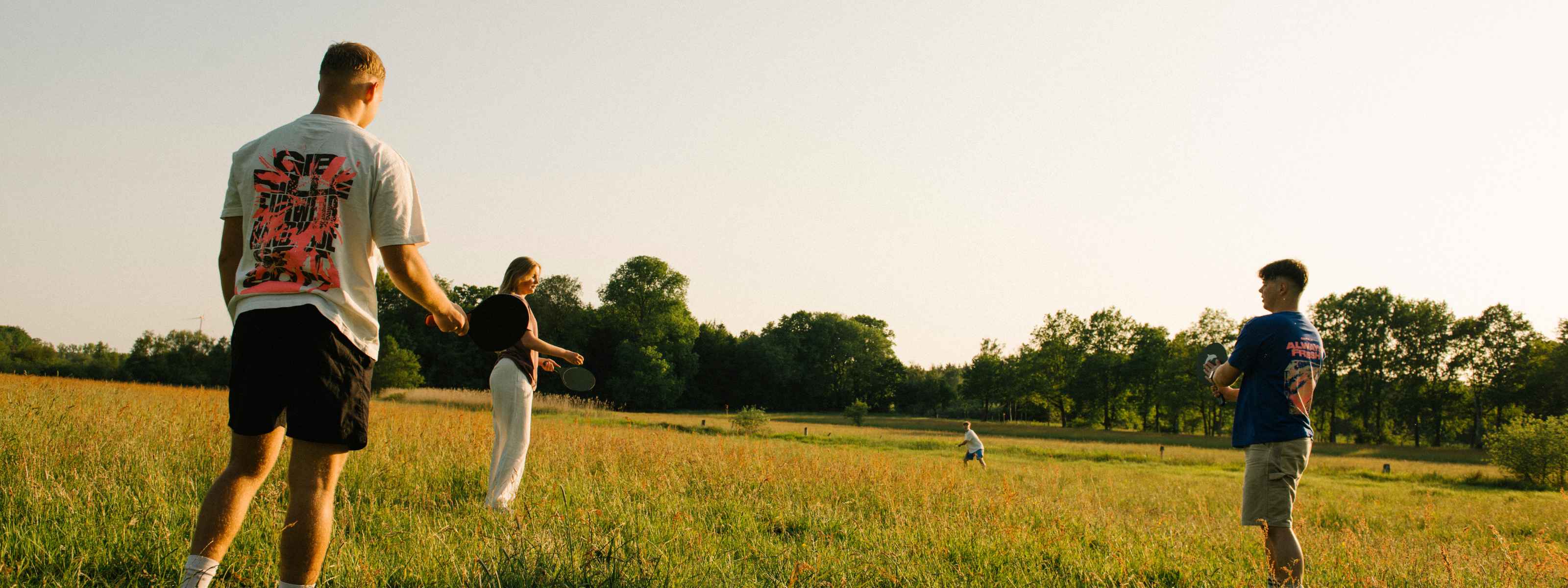 Gib Rillé Nachhaltigkeit-Shooting mit drei Personen auf einer Sommerwiese, umgeben von Natur, die nachhaltige Textilien mit einem modernen Graphic Print tragen.